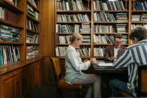 Group of students studying together in a cozy library setting with bookshelves around.